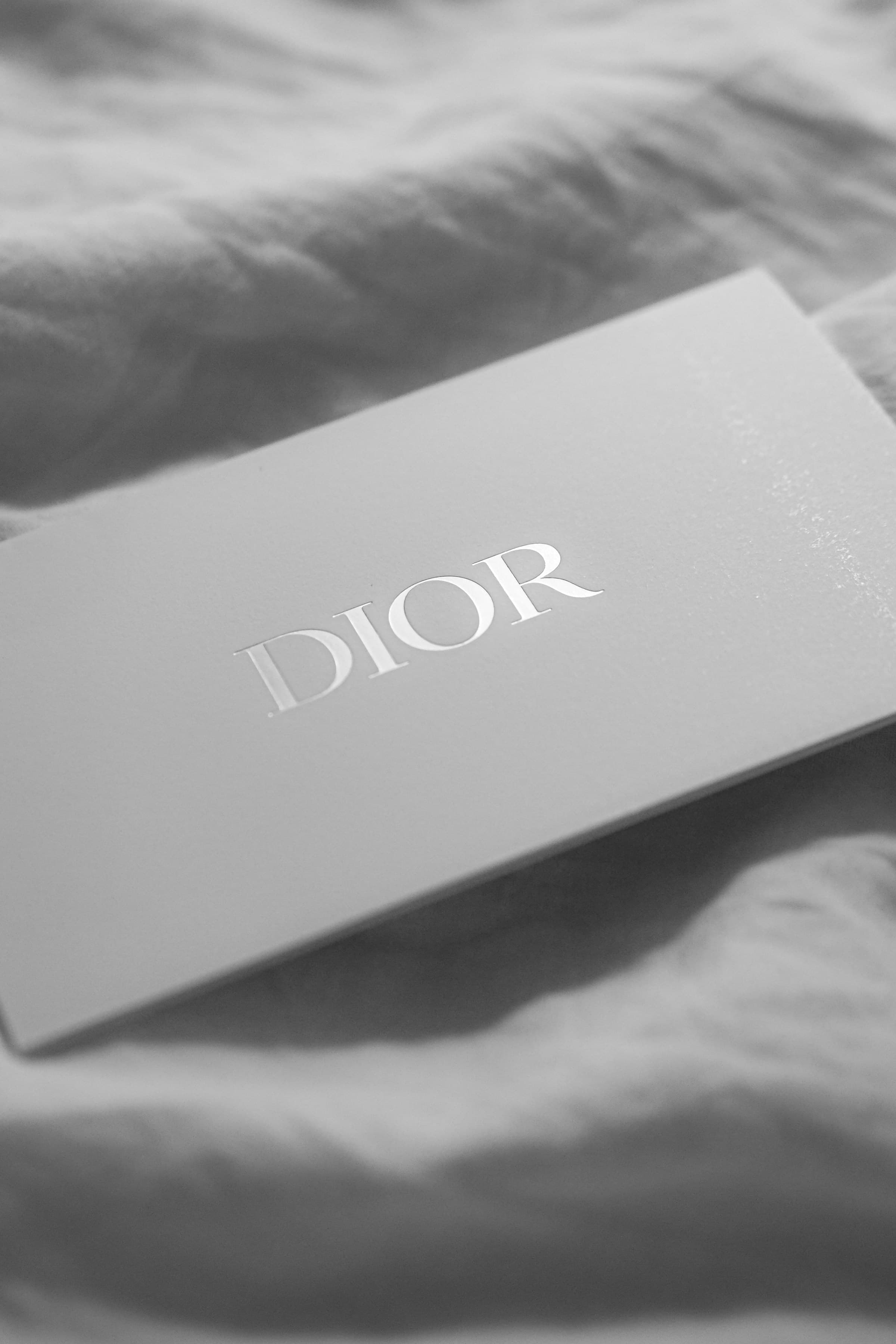 Embossed Dior logo on a white brand card resting on linen fabric