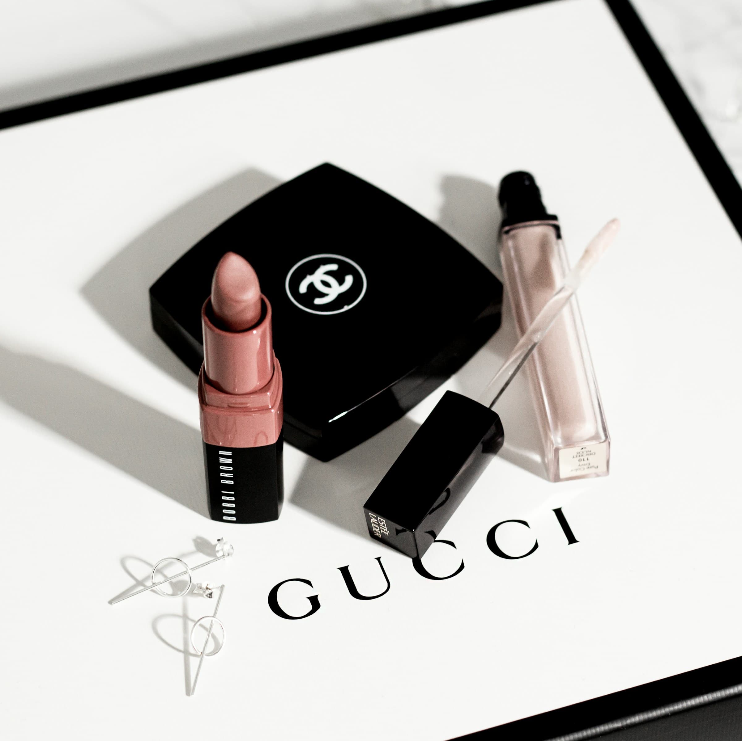 Editorial flat lay of Chanel, Gucci, Bobbi Brown, and Estée Lauder luxury beauty products