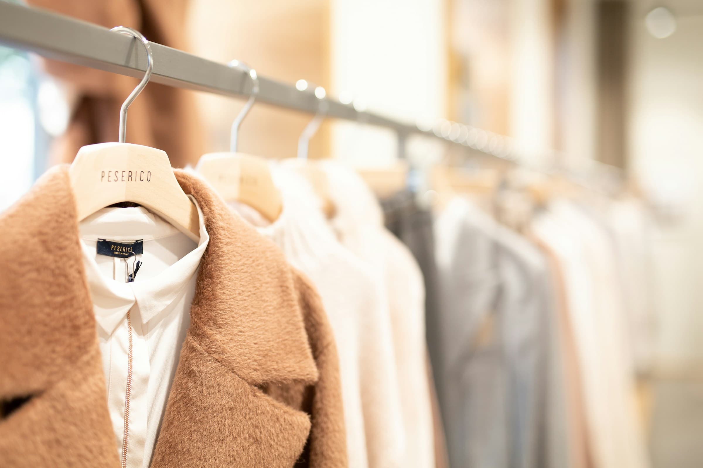Luxury camel coat and white shirt on a wooden hanger inside a premium boutique