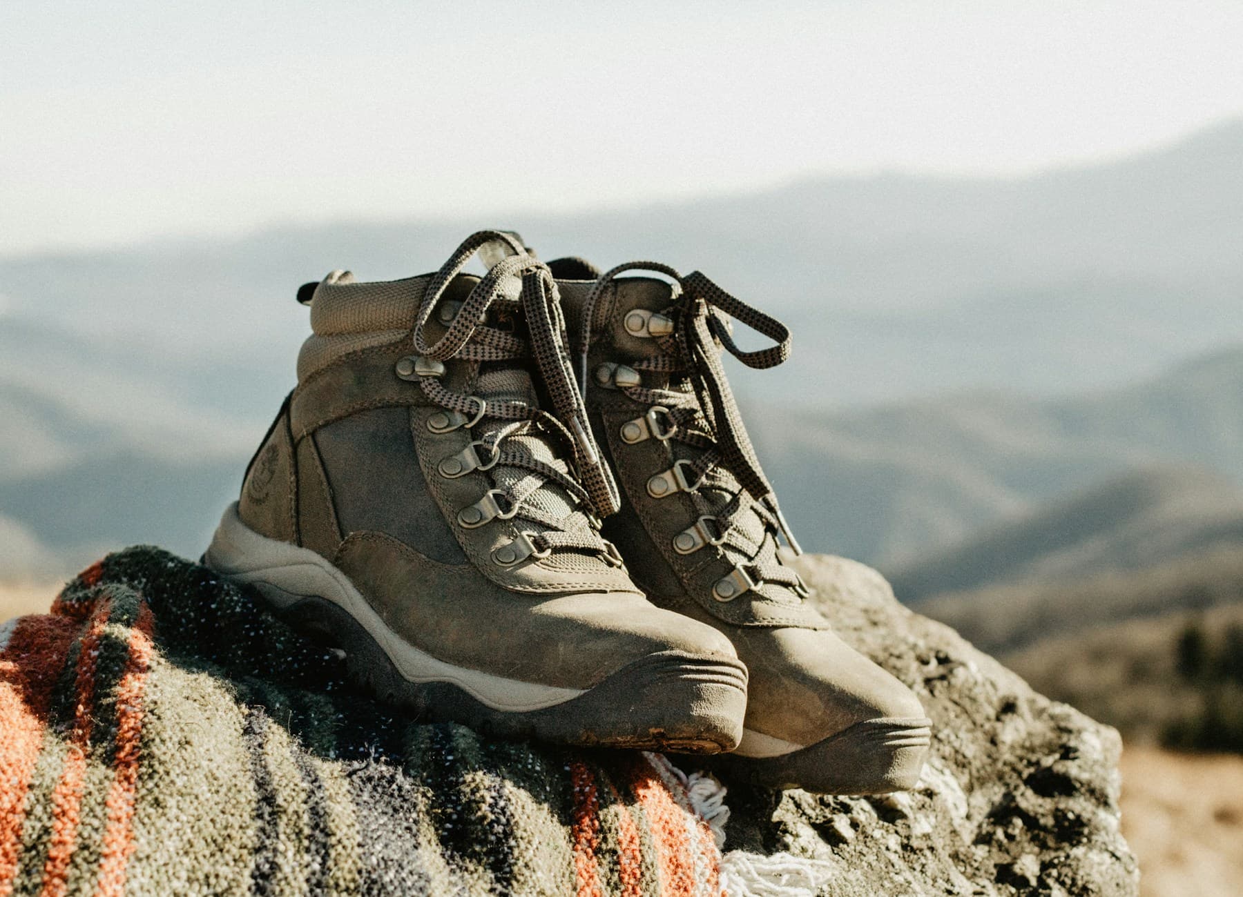 Worn leather hiking boots with visible brand mark resting on a sunlit rock overlooking mountains